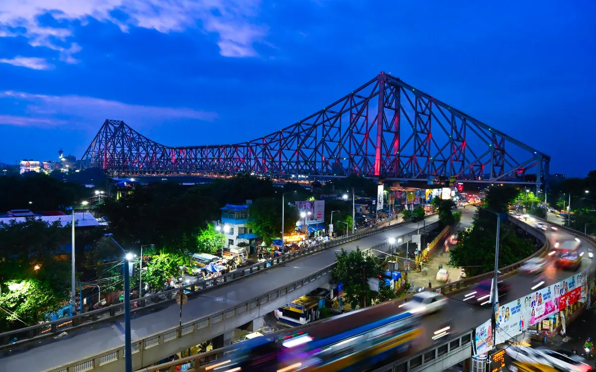 Howrah Bridge lit up at dusk above busy city traffic in Kolkata