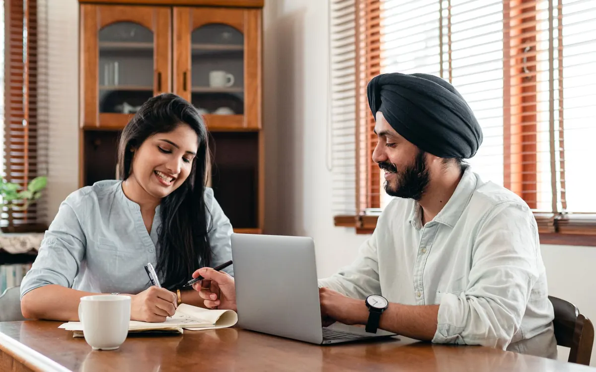 Two colleagues at a wooden table planning a campaign together on a laptop and notebook